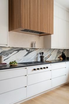 a kitchen with white cabinets and marble counter tops, along with wooden shelves on the wall