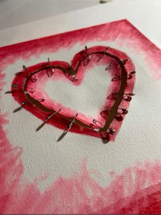 a heart with pins stuck in it on top of a piece of paper that has been dyed pink and white