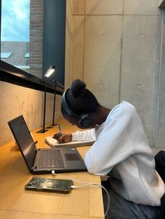 a person sitting at a desk with a laptop and headphones on, writing in a notebook