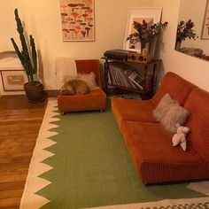 a living room with two orange couches and a green rug on the wooden floor