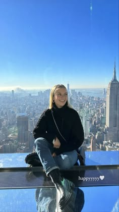 a woman sitting on top of a tall building in new york city, looking at the camera