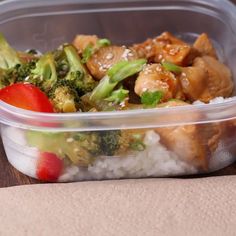 a plastic container filled with rice, broccoli and chicken on top of a wooden table