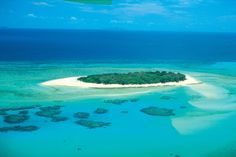 an island in the middle of water surrounded by sand and corals with blue sky