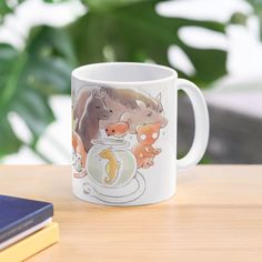 a coffee mug sitting on top of a wooden table next to a book and plant