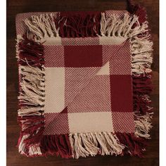 a red and white checkered blanket with fringes on the bottom, sitting on a wooden floor