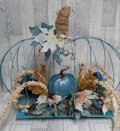 a blue pumpkin is sitting in a wire basket with leaves and flowers on the side