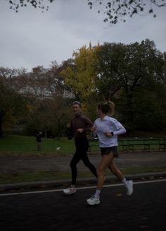 a man and woman running down the street in front of some trees on a cloudy day