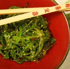 a red bowl filled with greens and chopsticks