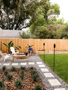 a man sitting on a chair in the middle of a yard next to a wooden fence