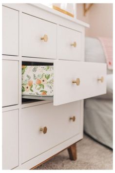 a white dresser with drawers and flowers on the drawer pulls in front of a bed