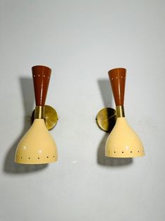 two yellow and brown wall lights on a white wall next to each other with one light turned off