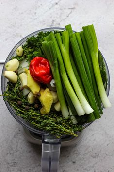 a blender filled with green vegetables on top of a white counter next to a red pepper