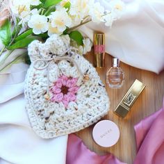 a crocheted bag, perfume and flowers on a table