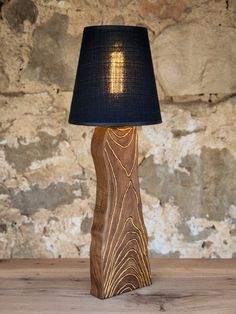 a wooden table lamp with a black shade on it and a stone wall in the background