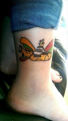 a woman's foot with a cartoon character tattoo on her left side leg, and a yellow surfboard in the background