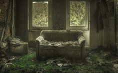 an old couch sitting in the middle of a living room filled with dirt and grass