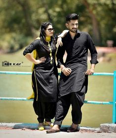 a man and woman standing next to each other on a bridge in front of water