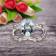 a ring with an aqua blue stone surrounded by white and clear diamonds sits on a table next to tulips