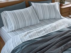 an unmade bed with blue and white striped comforter on top of it next to a night stand