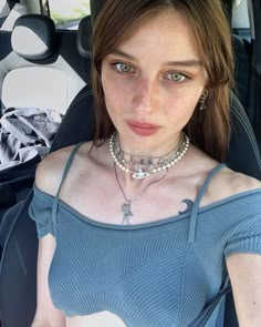 a woman sitting in the back seat of a car wearing a choker and pearls