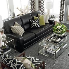 a living room with black leather couches and zebra print throw pillows on the floor