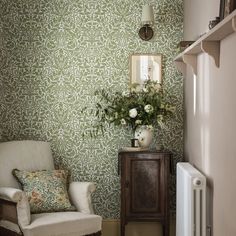 a white chair sitting next to a wall with green and white wallpaper on it