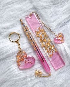 the pink pen is next to two heart shaped keychains and a gold chain