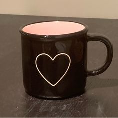 a black coffee mug with a white heart on the front and bottom, sitting on a table