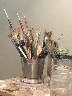 there are many paint brushes in the cup on the table next to the glass jar