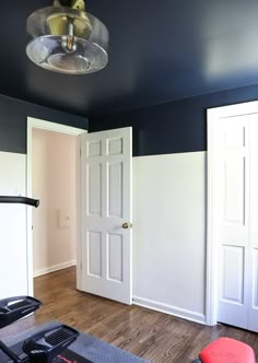 an empty room with white doors and hard wood flooring on one side, light fixture in the middle