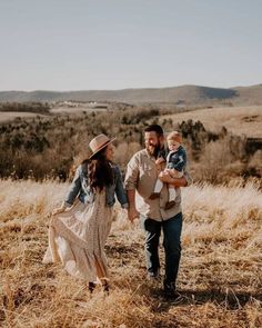 a man and woman walking through a field with a baby in their arms while holding hands