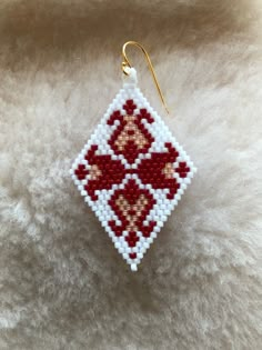 a small red and white beaded ornament hanging from a gold - plated hook