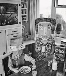 two dolls sitting at a table with food and milk in front of them, one holding a cup