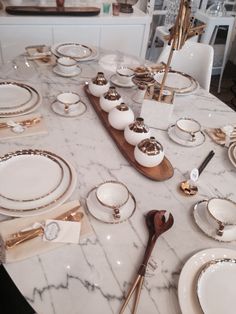 a marble table topped with white plates and gold trimmed place settings on top of it