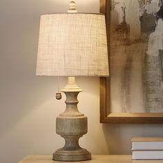 a table lamp sitting on top of a wooden dresser next to a painting and a mirror