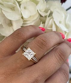 a close up of a person's hand with a ring and flowers in the background