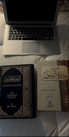 an open laptop computer sitting on top of a bed next to two books and a notebook