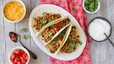 three tacos are sitting on a plate next to bowls of salsa and sour cream