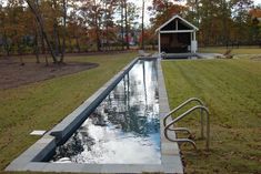 a small pool in the middle of a grassy area next to a house and trees