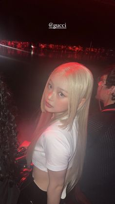 a girl with long blonde hair standing in front of a crowd at a concert, looking off to the side