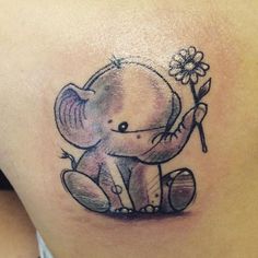 an elephant tattoo on the back of a woman's shoulder, with a flower in its trunk