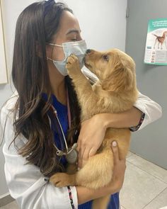 a woman wearing a face mask and holding a brown dog in her arms while she wears a stethoscope