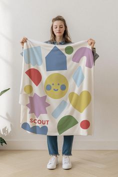 a woman holding up a white towel with colorful shapes on it