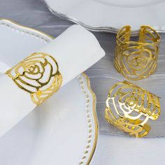 three napkin rings sitting on top of a plate next to a white and gold place setting