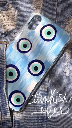 an iphone case with blue and green eyeballs on it, sitting on some jeans