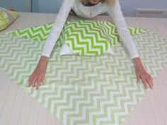 a woman laying on top of a green and white chevroned bed sheet with her hands in the air