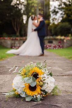 a bride and groom standing in front of a sunflower bouquet on a stone path