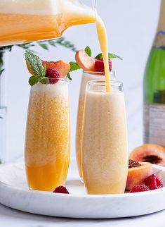 two glasses filled with fruit and juice being poured into them