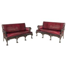 a pair of red leather sofas with carved wood legs and arms, on white background