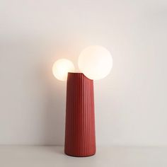 a red vase sitting on top of a table next to a white wall with two lights